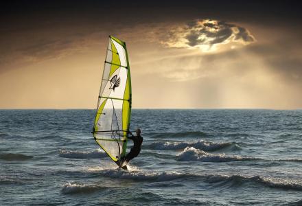 Someone windsurfing with god rays behind